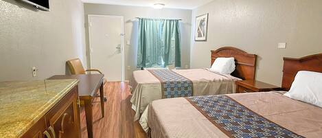 Habitación de hotel con dos camas, un escritorio, una silla y un televisor en la pared.