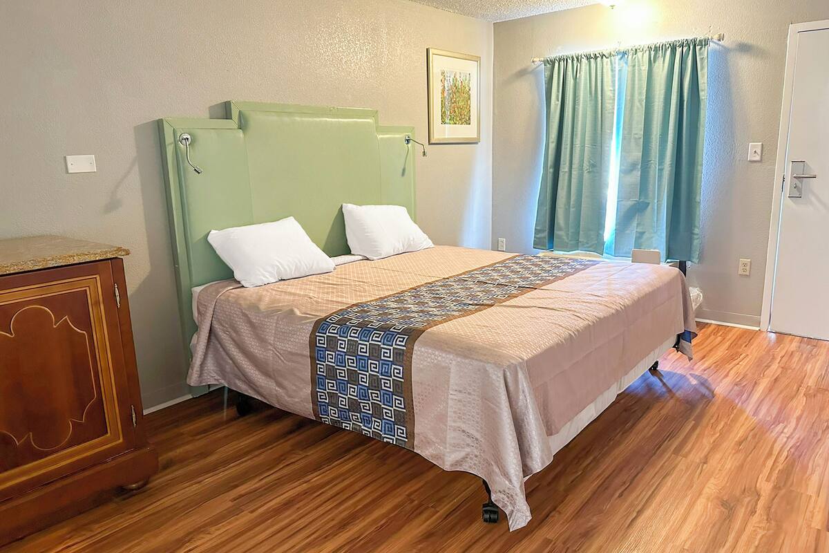 Un dormitorio con cama, piso de madera, cabecero verde y ventana con cortinas.