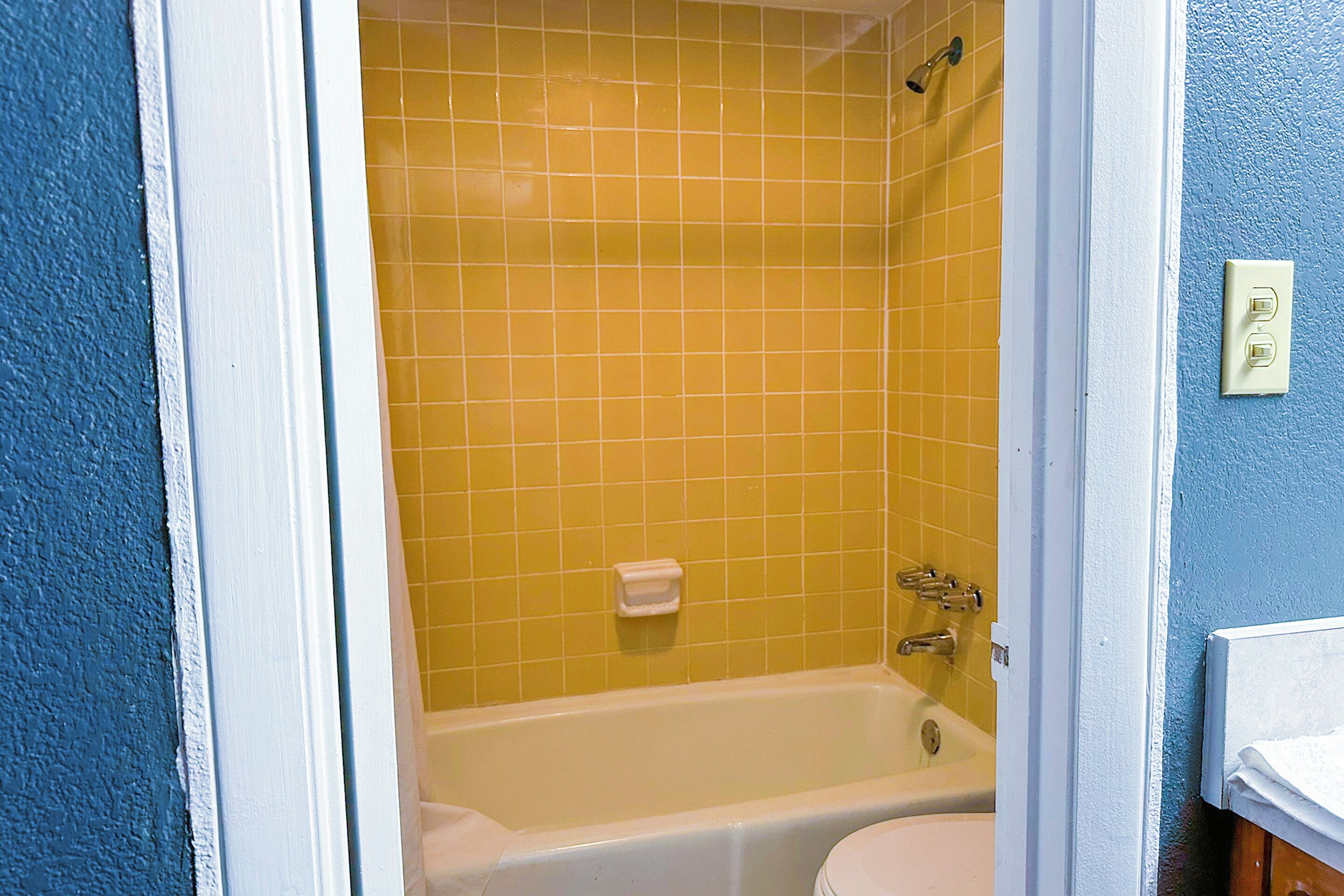 A bathroom with a bathtub, a toilet, and yellow tiled walls.