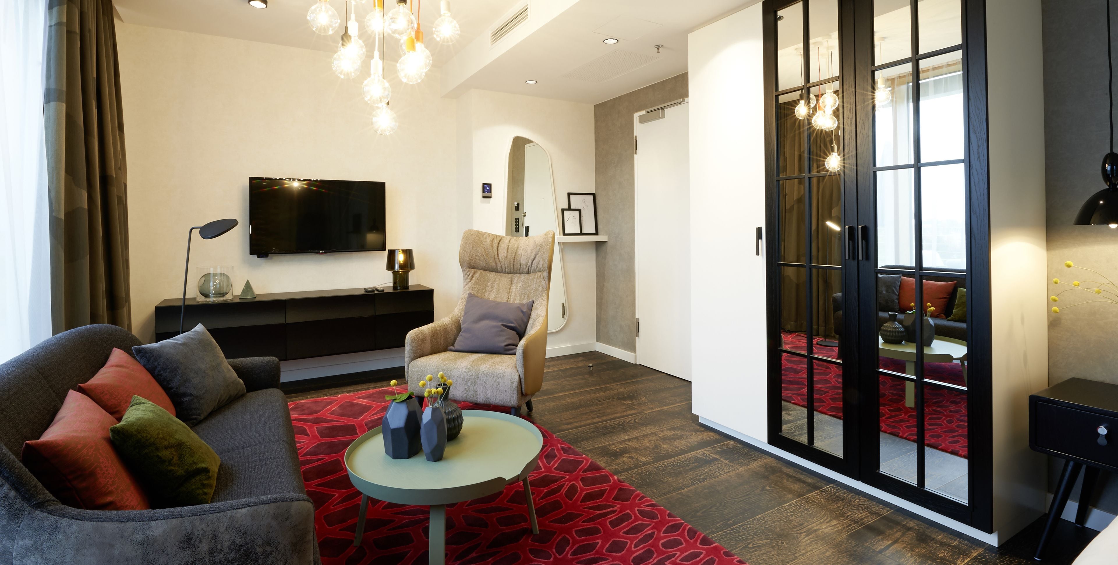 Un salon moderne avec un canapé gris, un tapis à motifs rouges et une table basse ronde agrémentée de vases.