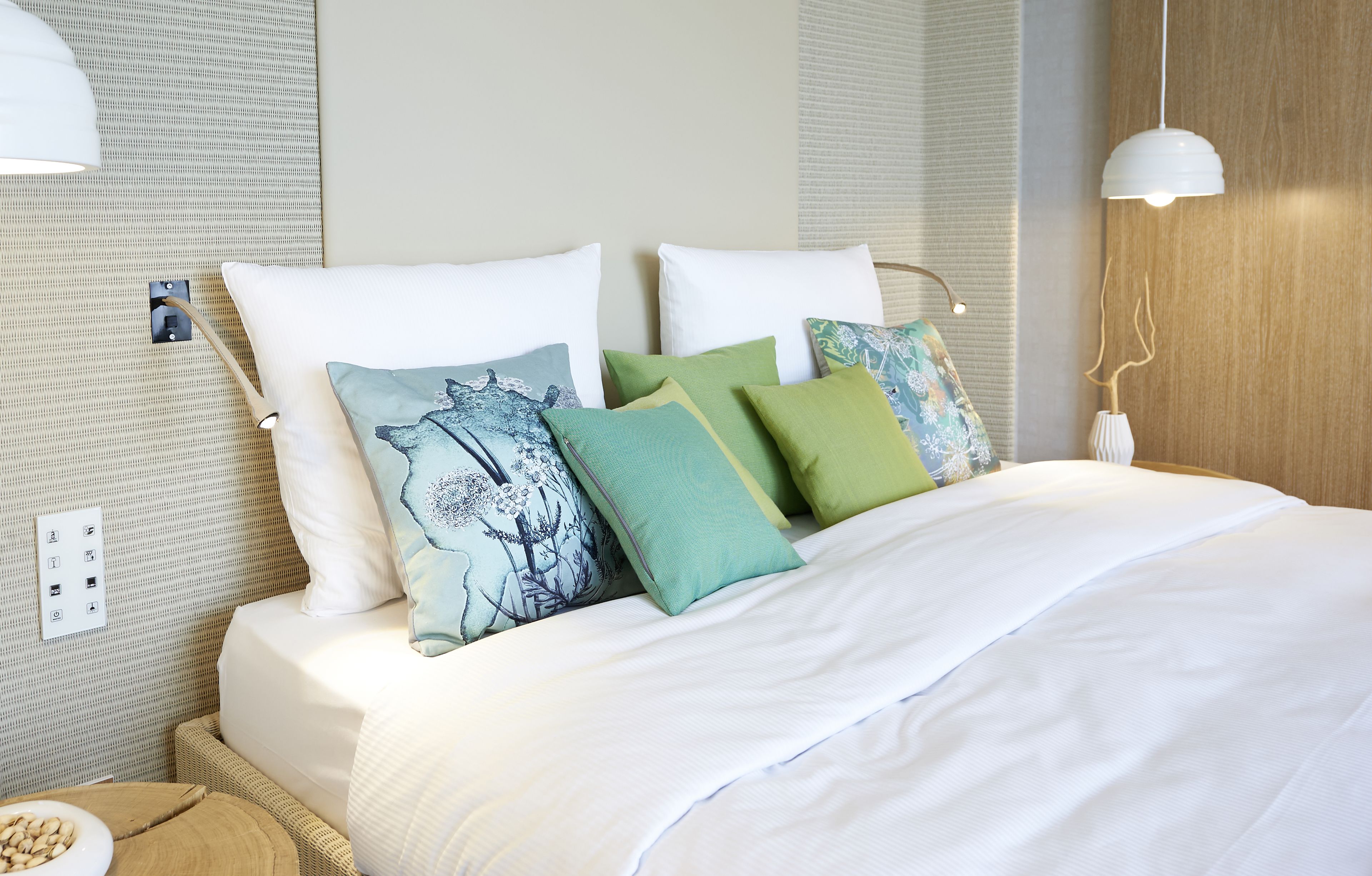 Una cama bien hecha con ropa blanca y varias almohadas de distintos colores.