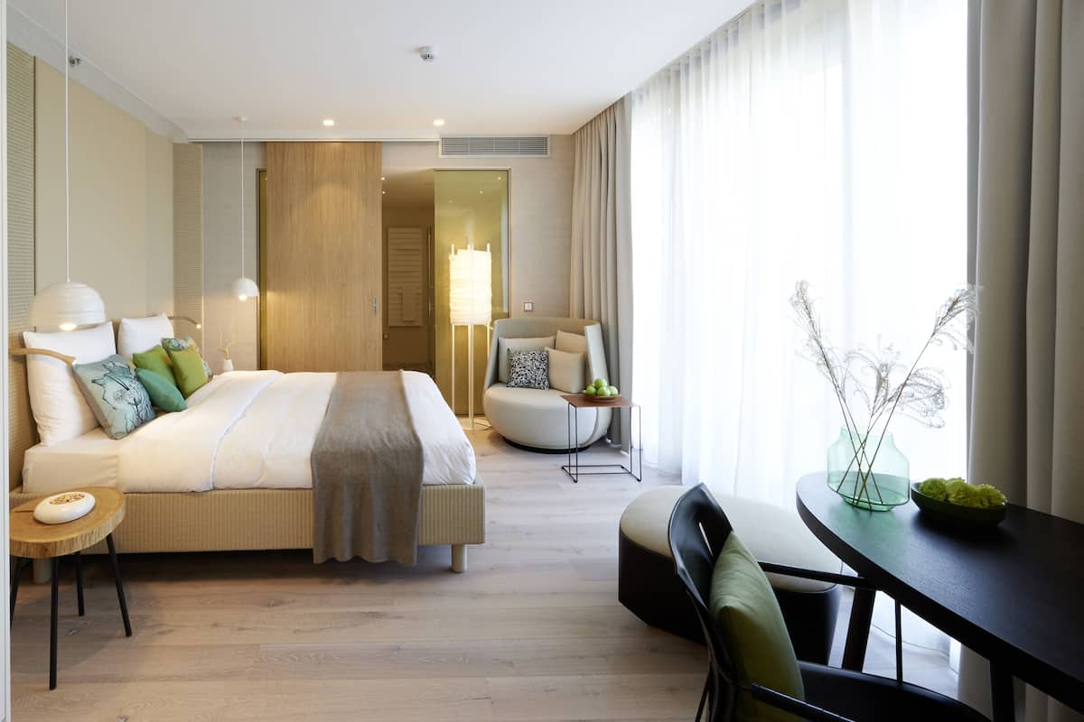 Ein modernes Hotelzimmer mit einem großen Bett, einer Sitzecke mit Tisch und Blick ins Freie.
