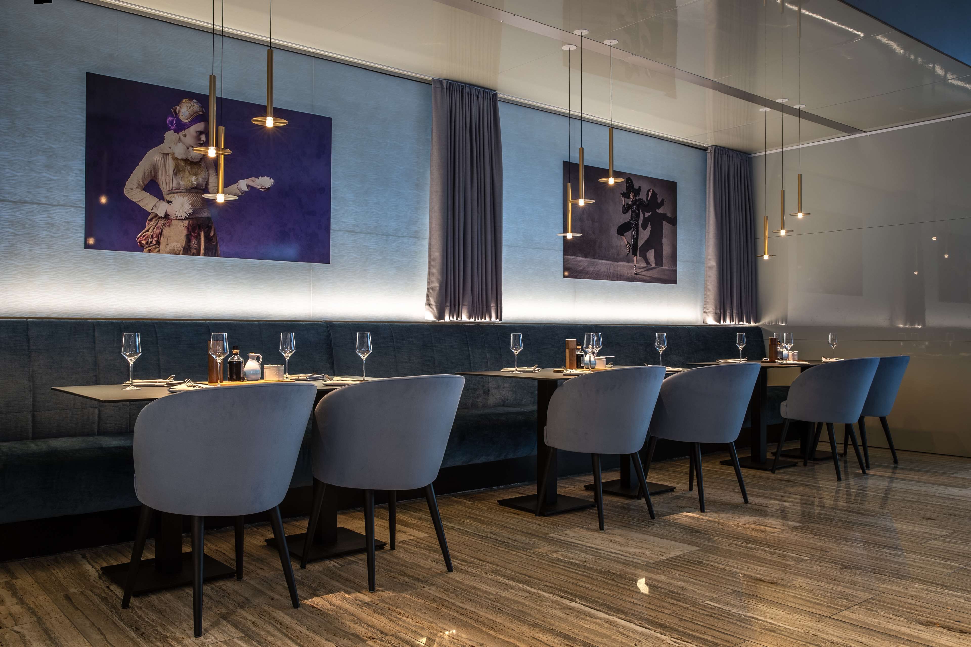 Un restaurante moderno con una barra larga, sillas azules y lámparas colgantes.