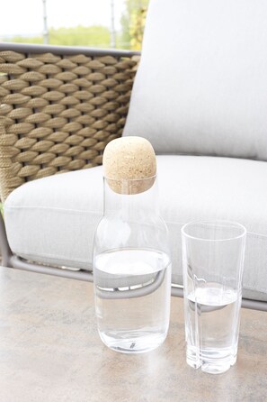 A clear glass bottle with a cork stopper and two clear glasses on a table.
