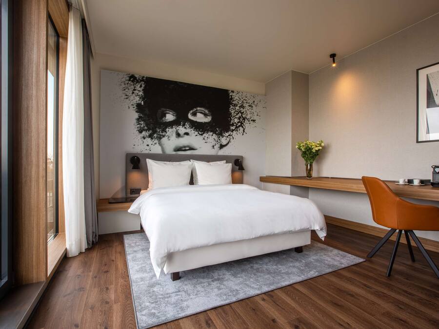 A modern bedroom with a large bed, a desk, and a window.
