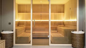 Un sauna avec des bancs en bois et des portes en verre, deux paniers en osier et un luminaire au plafond.