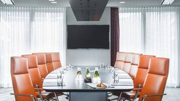 A conference room with a round table, orange leather chairs, and a flat-screen TV on the wall.