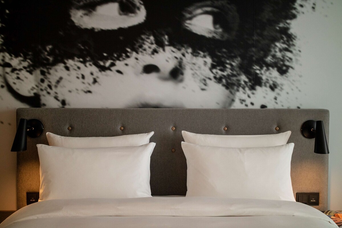 A bed with a grey upholstered headboard, two white pillows, and black wall sconces.