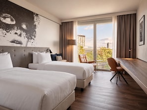 A hotel room with two beds, a desk, and a view of the city.