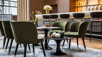 A modern bar area with green upholstered chairs, a round table, and a bar counter with bottles.