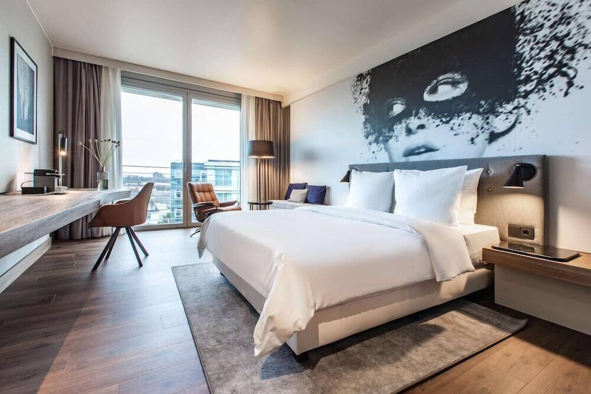 Ein modernes Hotelzimmer mit einem großen Bett, einem Schreibtisch und Blick auf die Stadt.