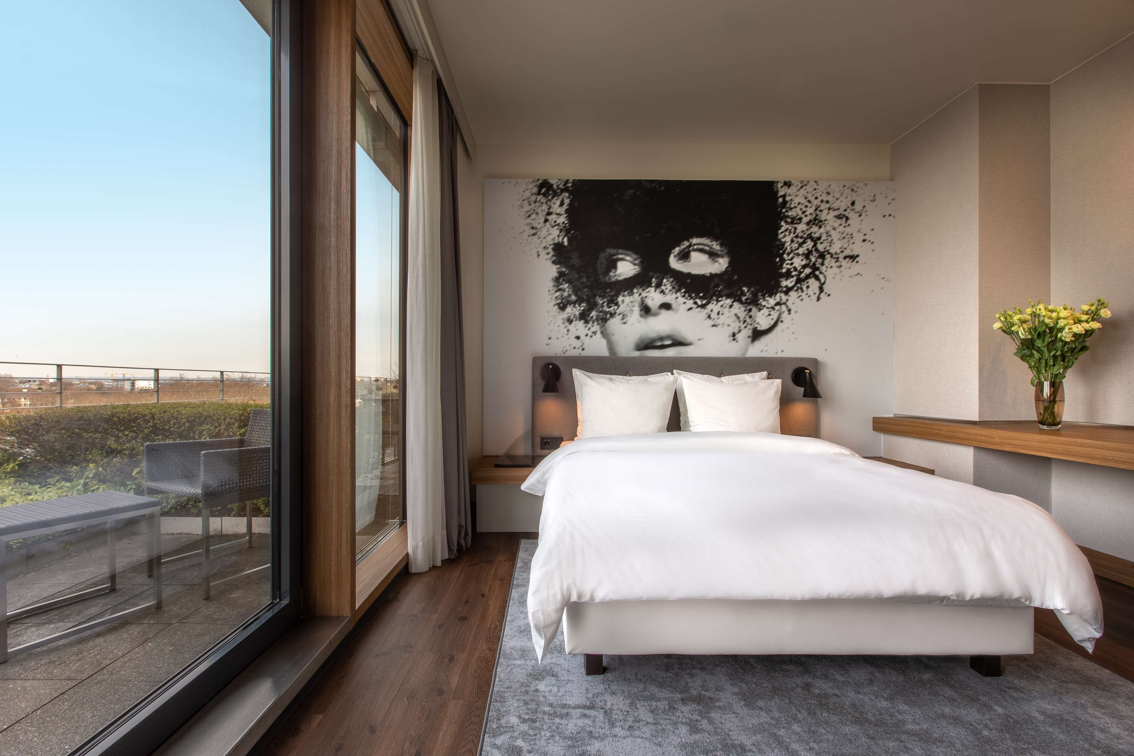 Ein modernes Schlafzimmer mit einem großen Bett, Blick ins Freie und einem einzigartigen Kunstwerk an der Wand.