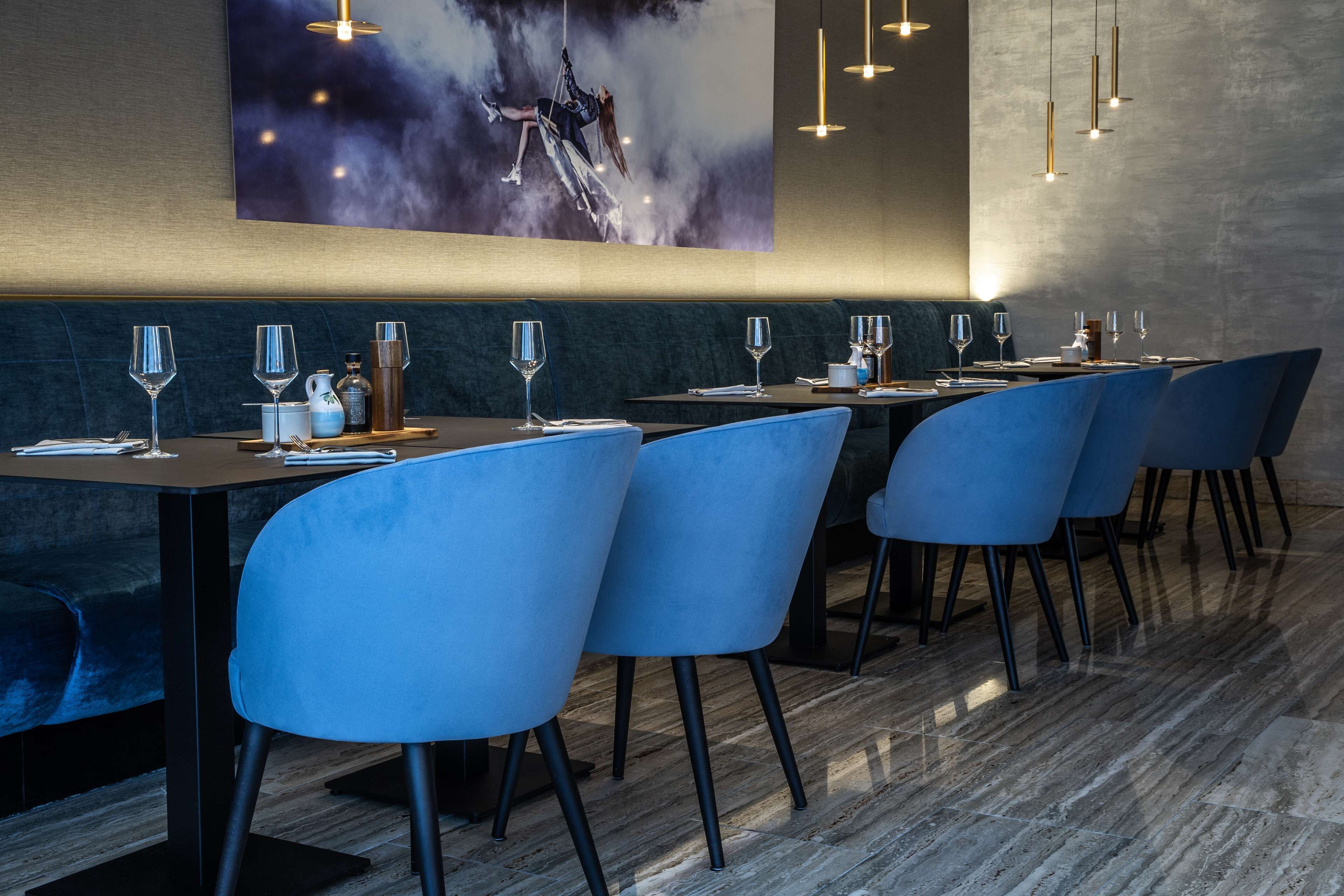 Un restaurante con una larga mesa dispuesta para comer, sillas azules y un cuadro abstracto grande en la pared.