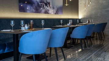 Un restaurante con una larga mesa dispuesta para comer, sillas azules y un cuadro abstracto grande en la pared.