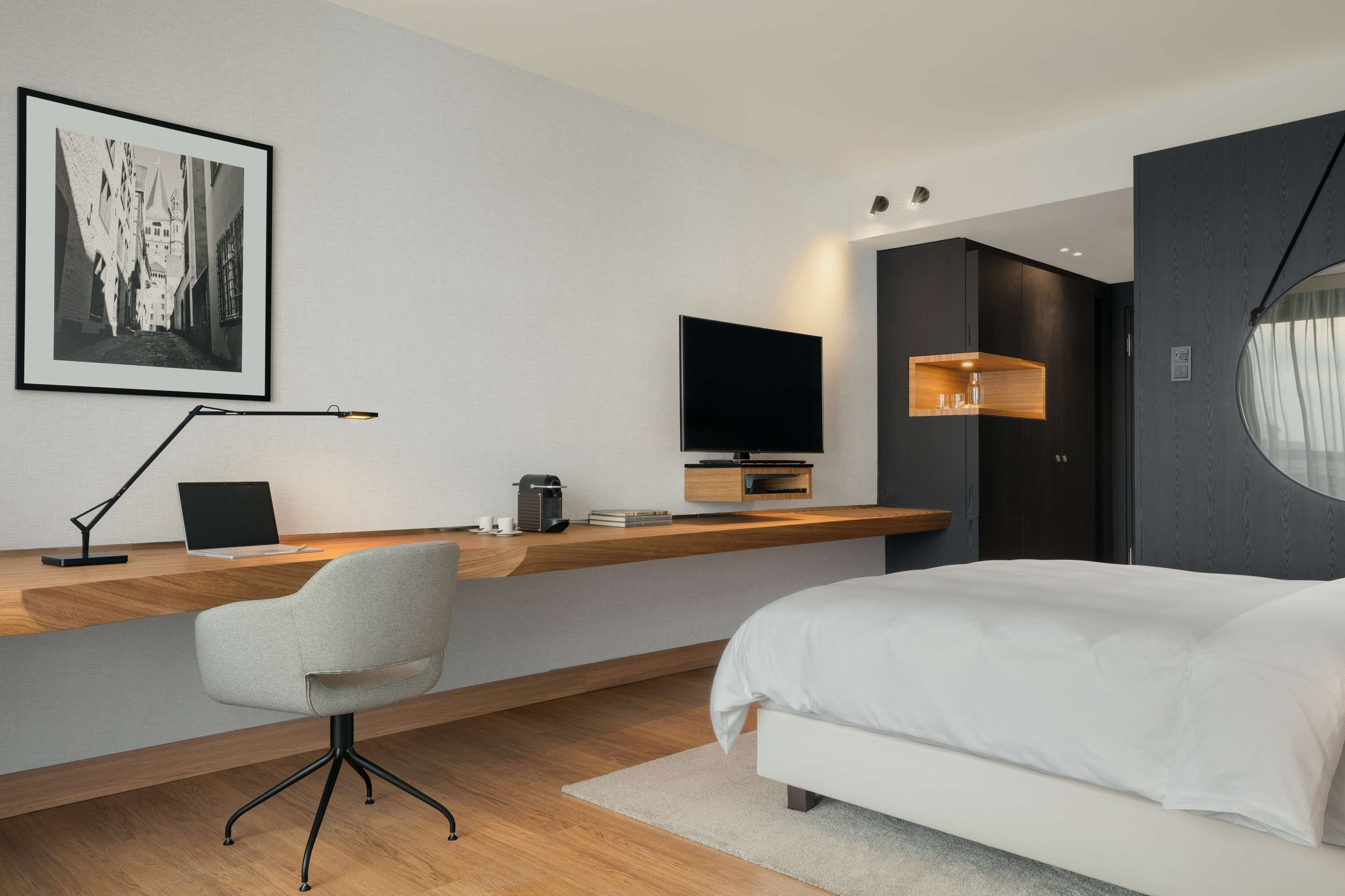 Habitación de hotel moderna con una cama grande, un escritorio con una computadora portátil, un televisor de pantalla plana y una obra de arte colgada.