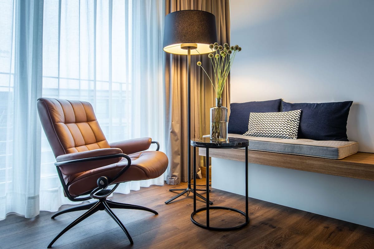 Ein modernes Zimmer mit Ledersessel, Beistelltisch mit Blumenvase, Lampe und Sofa mit gemusterten Kissen.