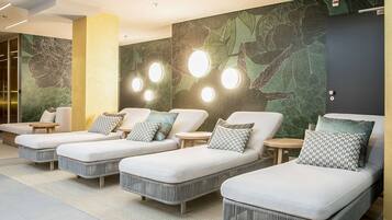 Relax in a serene spa room with a trio of lounge chairs, each paired with a small table and pillow, amidst a nature-inspired mural.