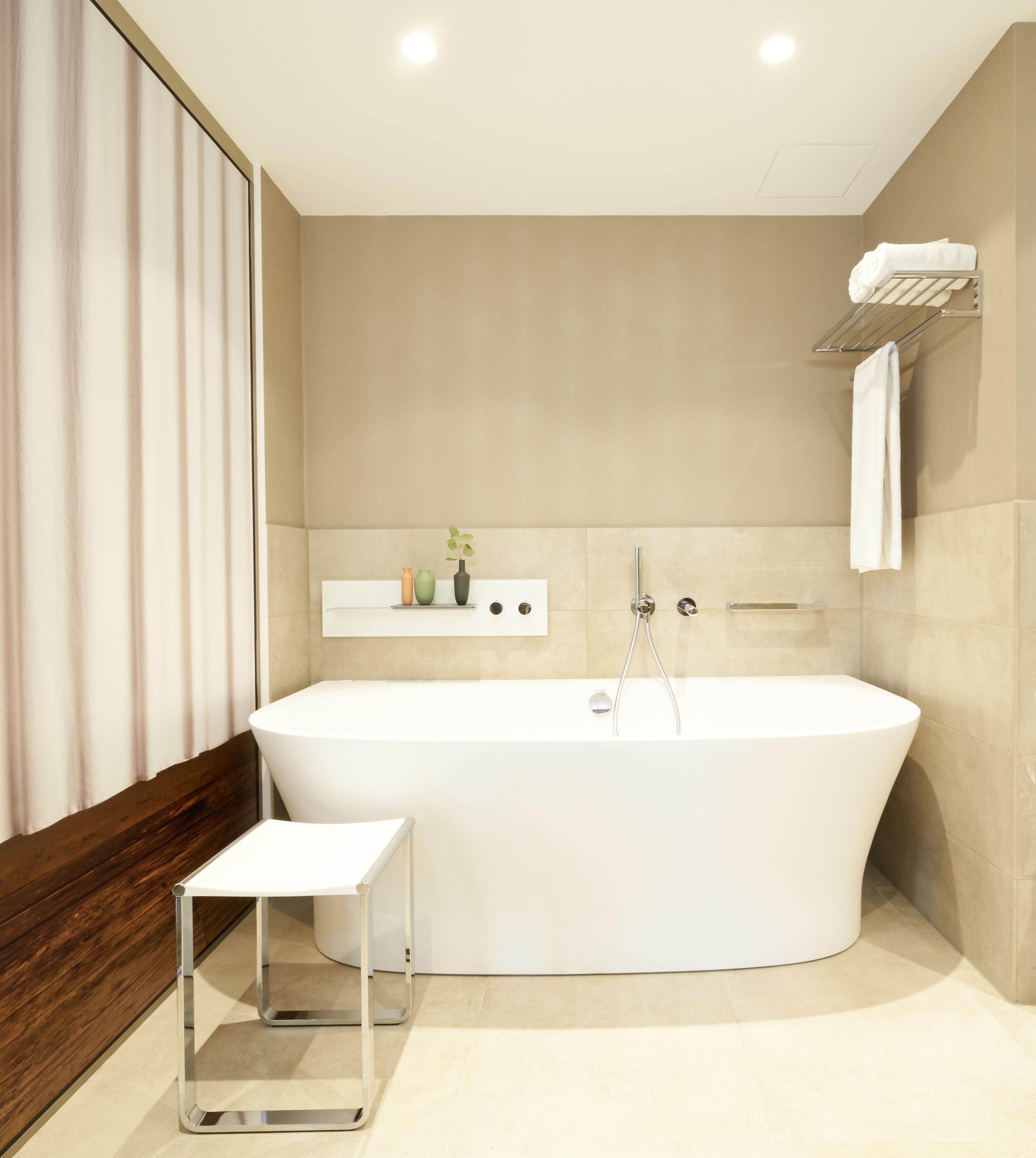 A modern bathroom with a freestanding bathtub, a small stool, and a shelf with decorative items.