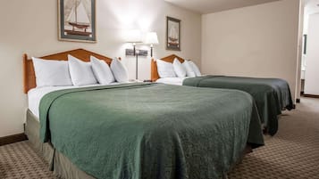 Une chambre d’hôtel avec deux lits, chacun doté d’une tête de lit en bois et d’une literie verte. Deux lampes murales et des tableaux encadrés sont accrochés au-dessus des lits.