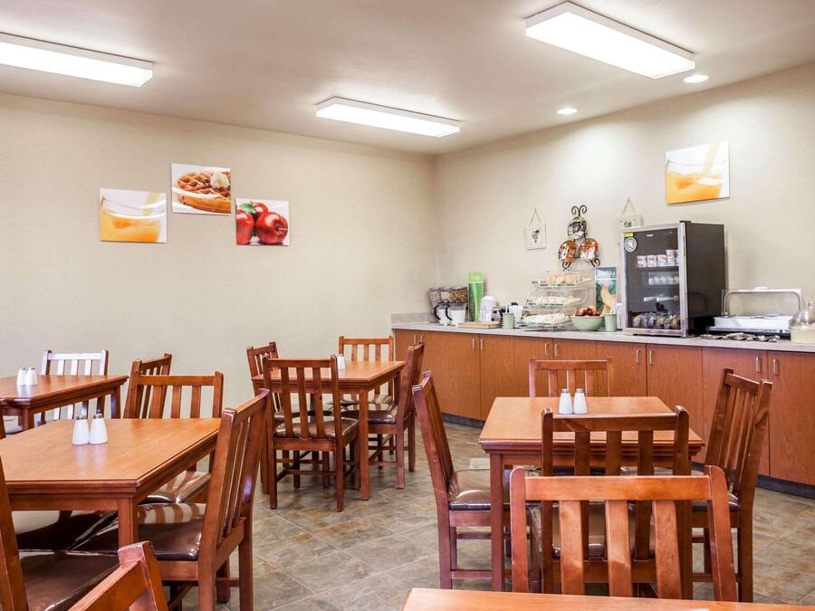 Comedor con mesas y sillas de madera, una encimera de cocina con diversos electrodomésticos y adornos en la pared que incluyen imágenes de comida.