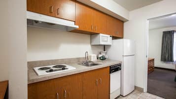 Una cocina compacta con armarios de madera, un microondas blanco, una estufa integrada, un fregadero y un lavavajillas.