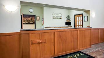 A reception desk with a clock, a framed picture, and a sign reading "Quality Inn & Suites by Choice Hotels".