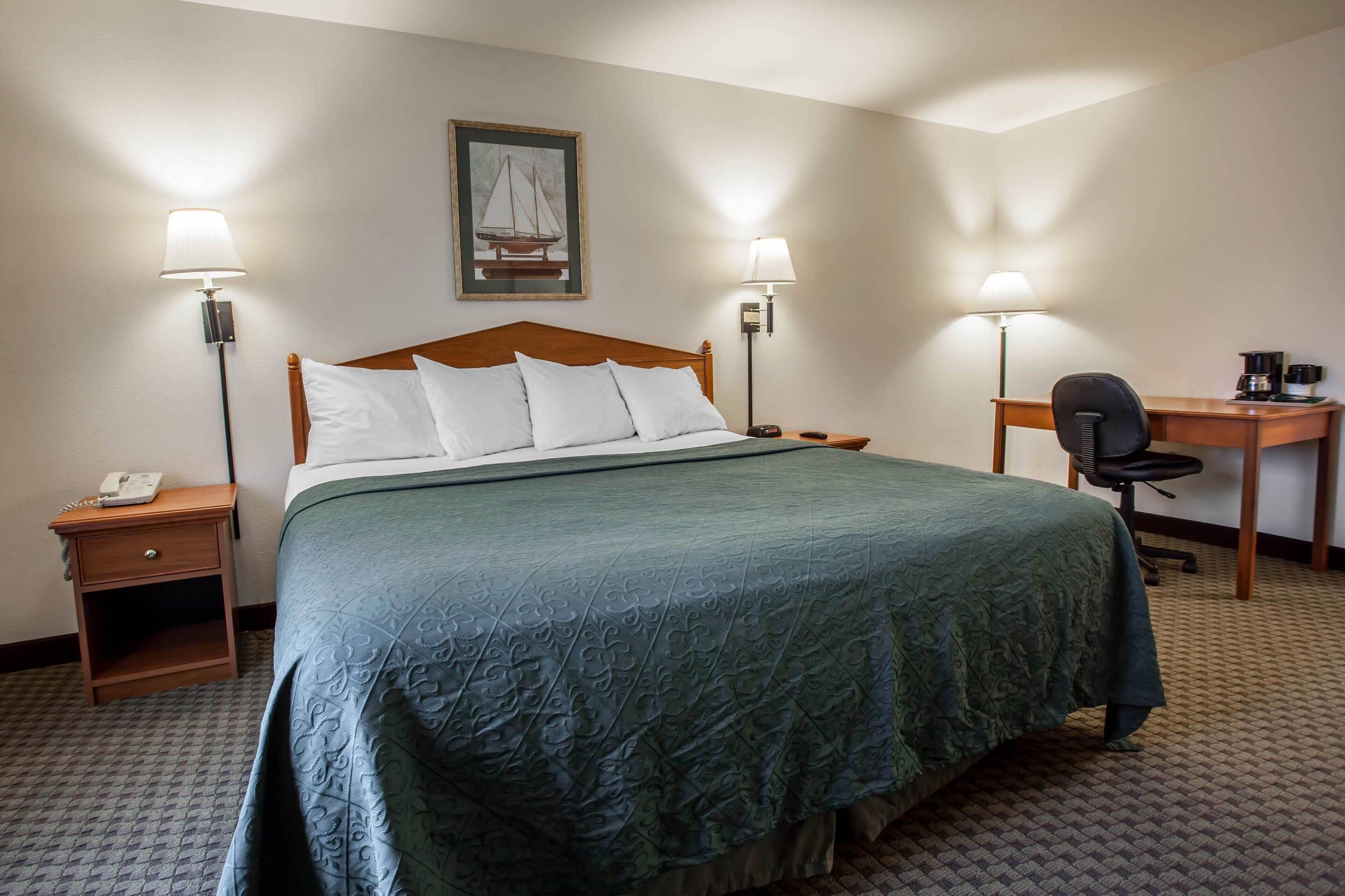Habitación de hotel con cama, dos lámparas de noche, un escritorio con silla y un cuadro en la pared.