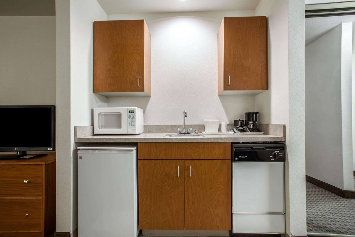 A compact kitchen with wooden cabinets, a microwave, a coffee maker, and a dishwasher.