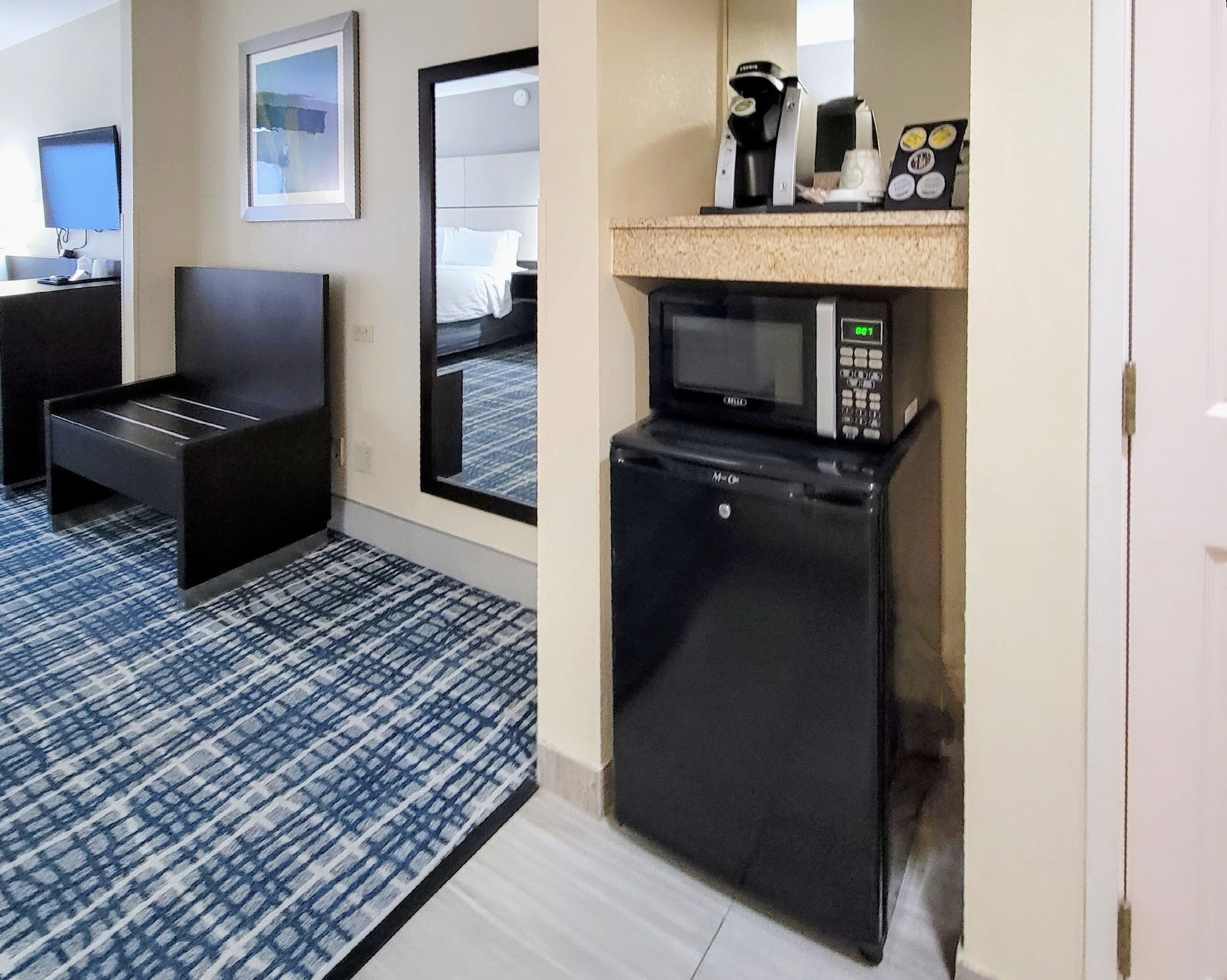 A compact hotel room with a kitchenette, a small seating area, and a television.