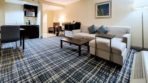 Una habitación de hotel con kitchenette, un sofá, una mesita de centro y una alfombra estampada.