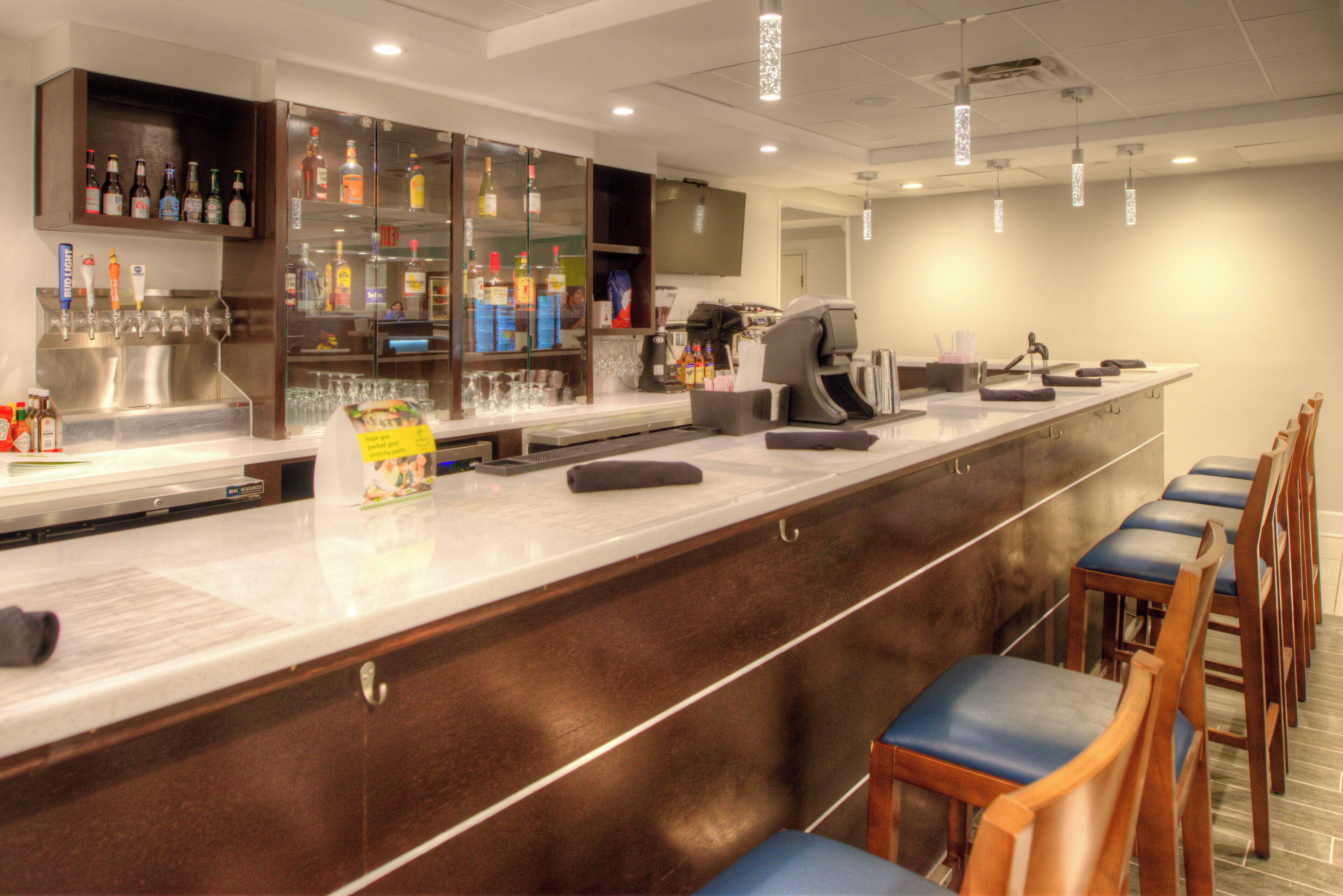 A bar area with a long counter, bar stools, and a variety of bottles and glasses.