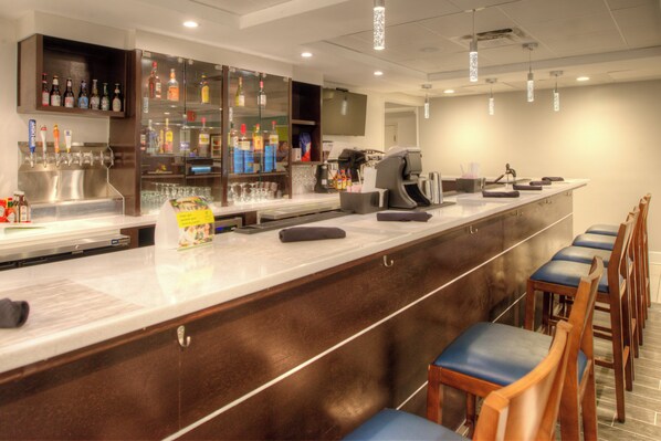 A bar area with a long counter, bar stools, and a variety of bottles and glasses.