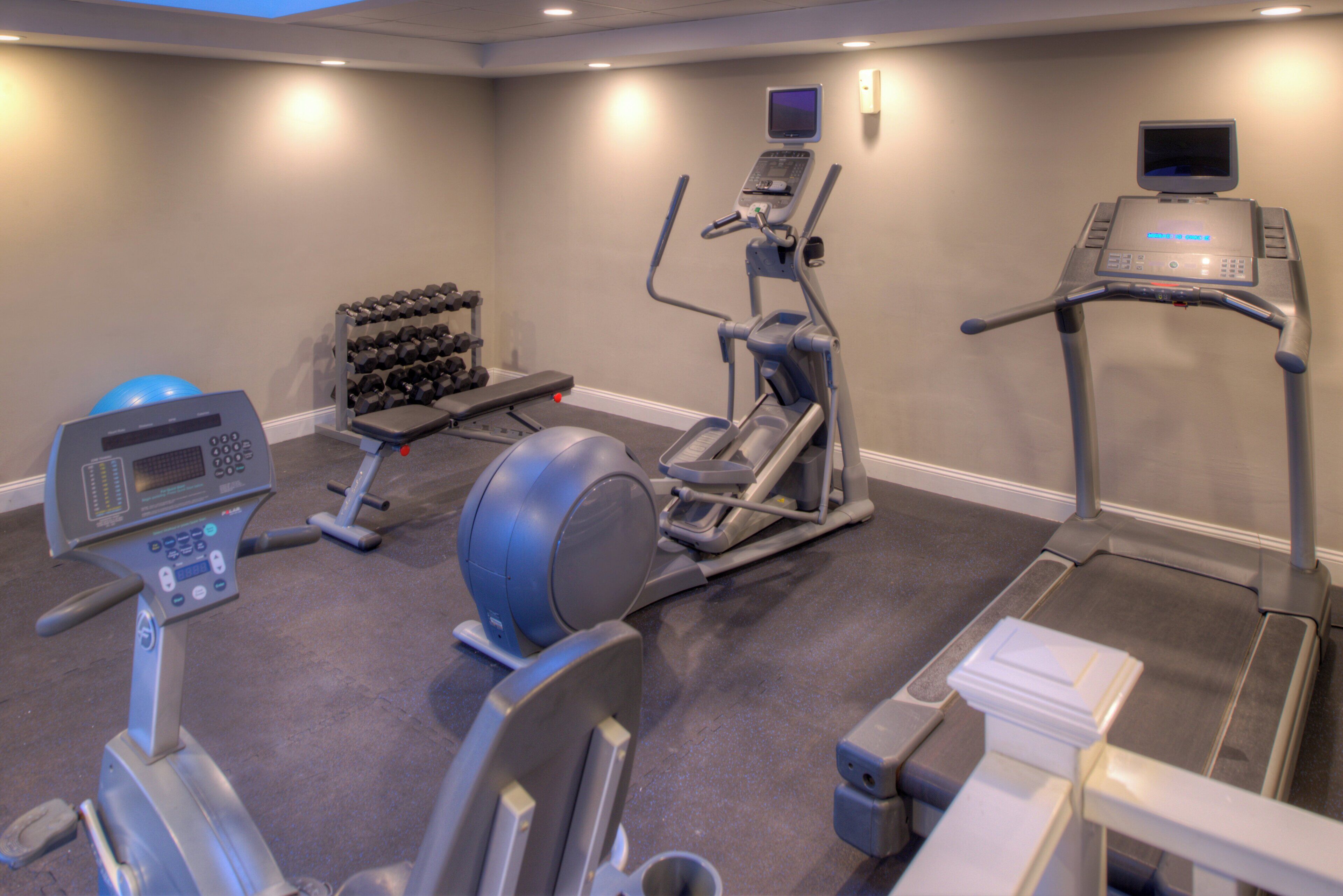 A gym with exercise equipment including a treadmill, elliptical, and weight bench.
