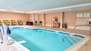 Una piscina interior con agua cristalina, una escalera de piscina y suelo de baldosas. Hay sillas y una pequeña mesa cerca de la piscina.