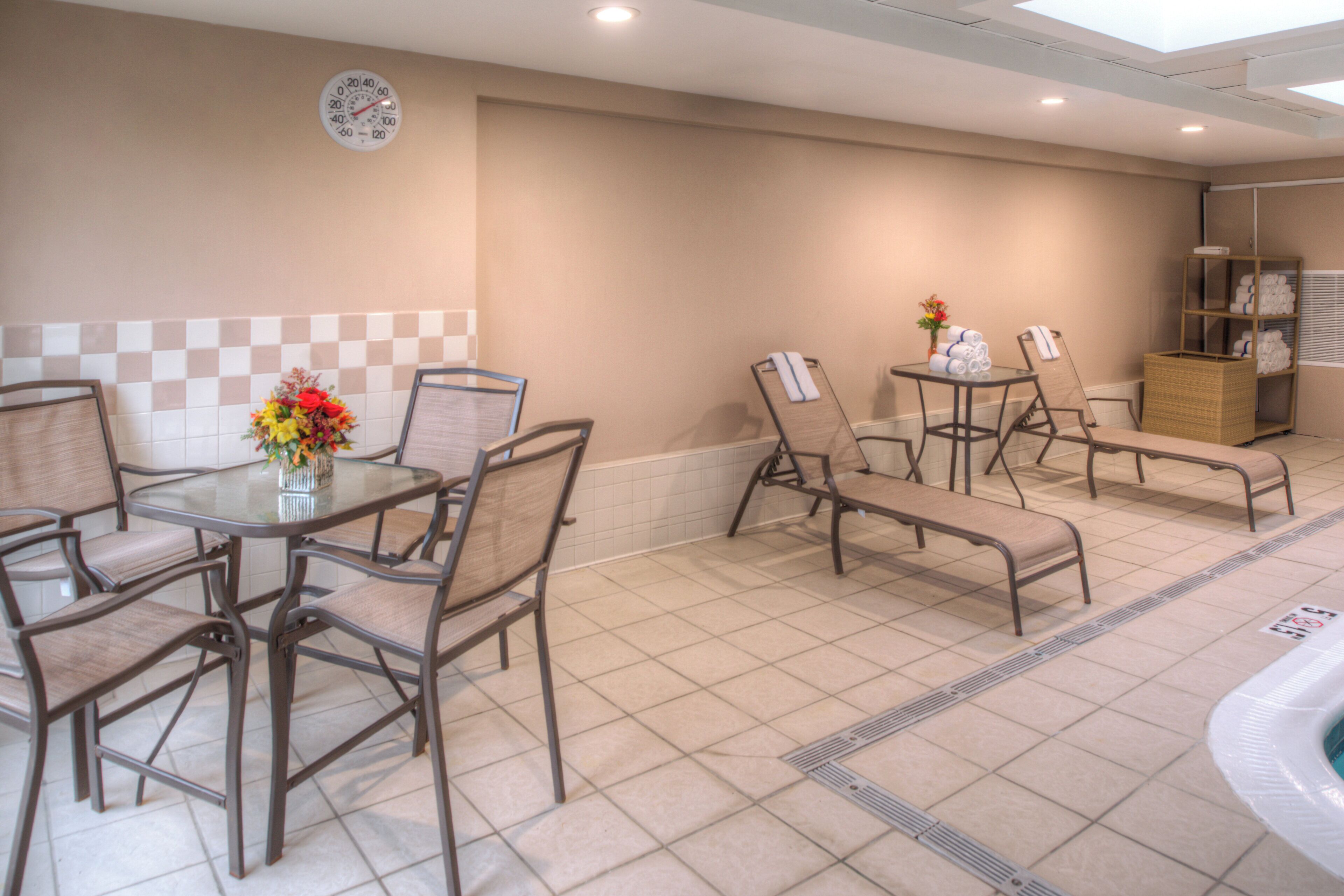 A hotel room with a checkered wall, a round table with chairs, a bench, and a small table with a vase of flowers.