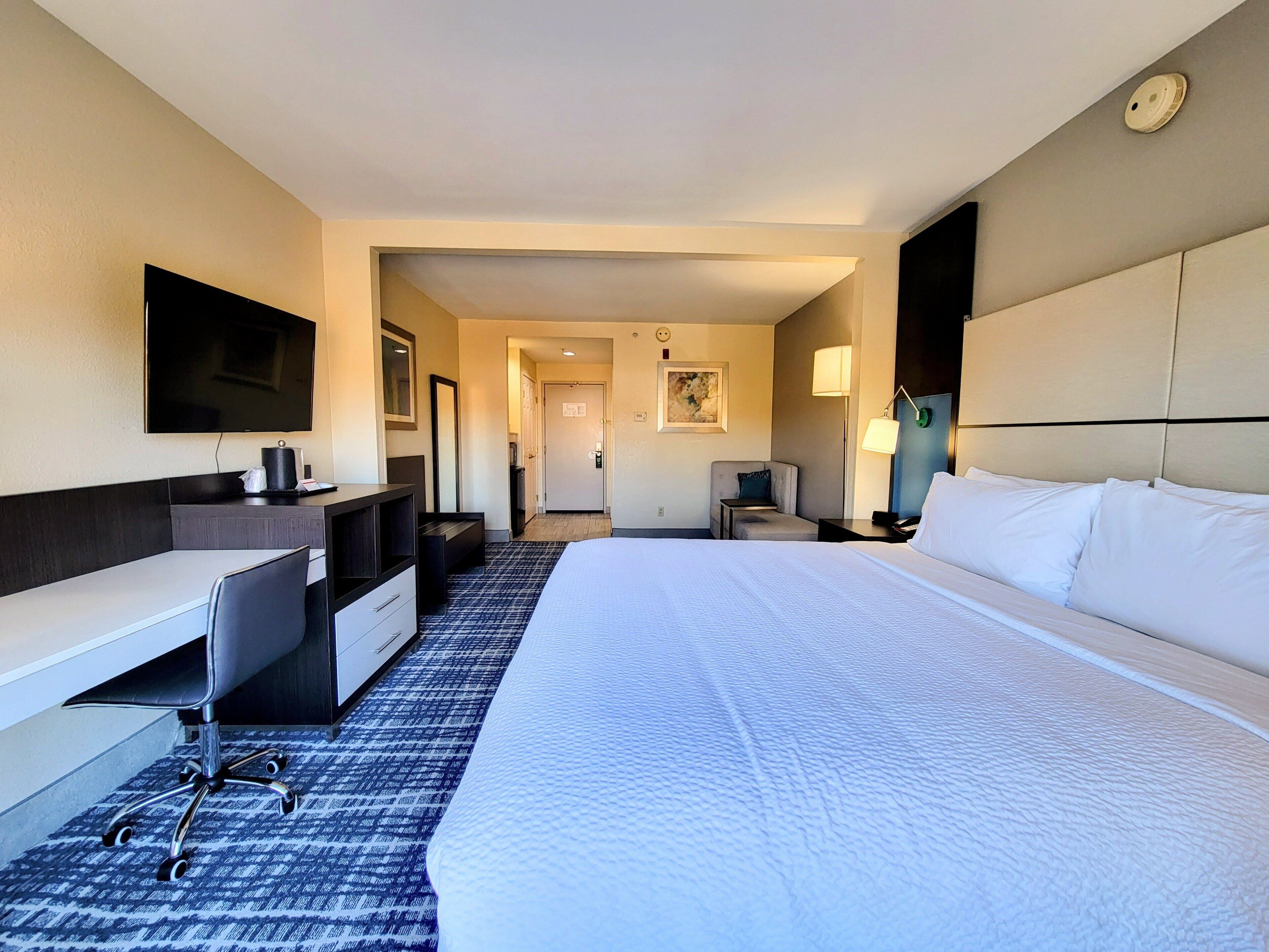 Una habitación de hotel con una cama grande, un escritorio, una silla, un televisor y una lámpara.