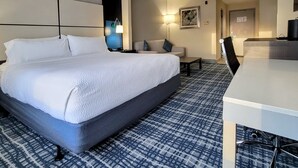 Una habitación de hotel con una cama grande, un escritorio, un sofá y una alfombra estampada.