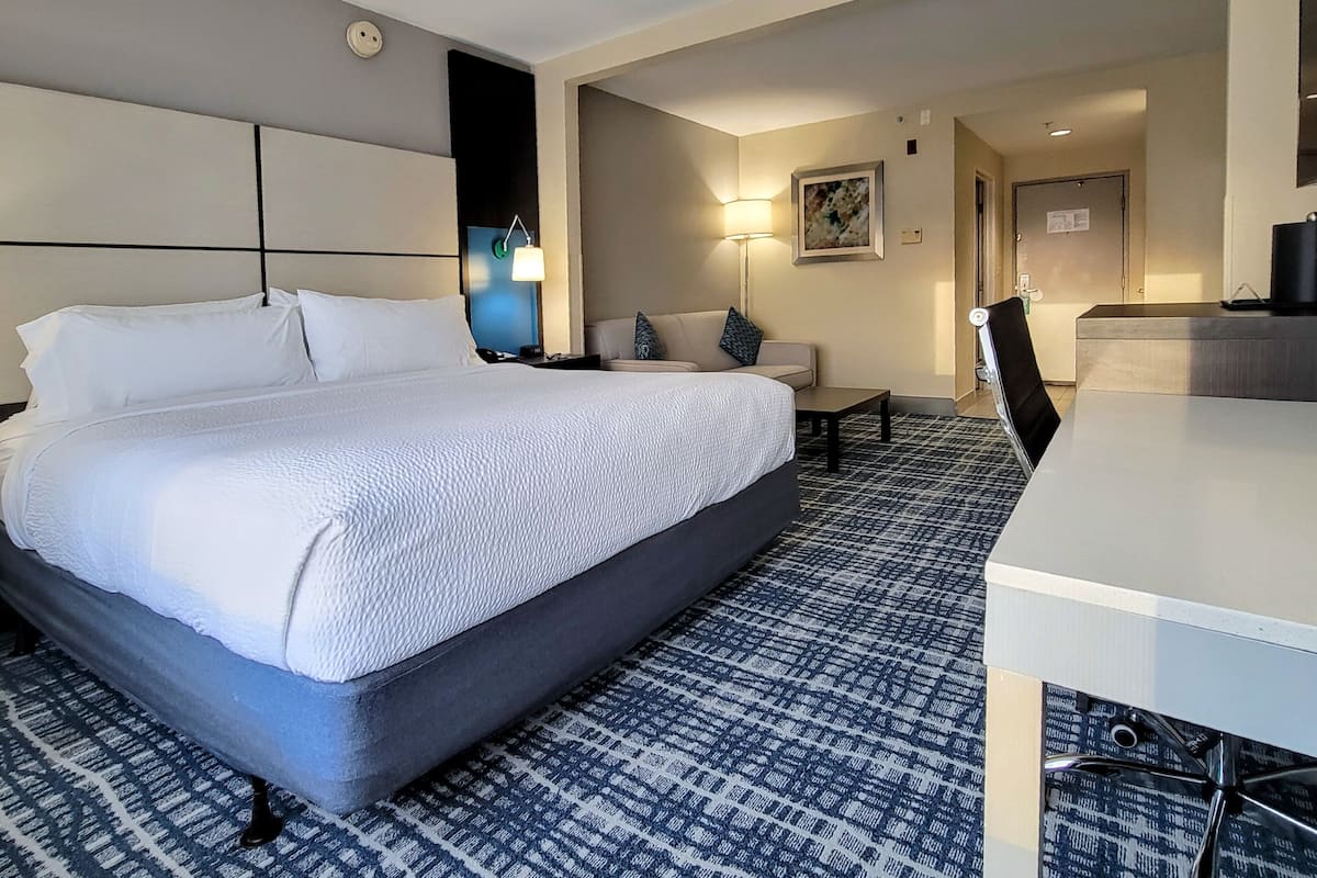 A hotel room with a large bed, a desk, a sofa, and a patterned carpet.