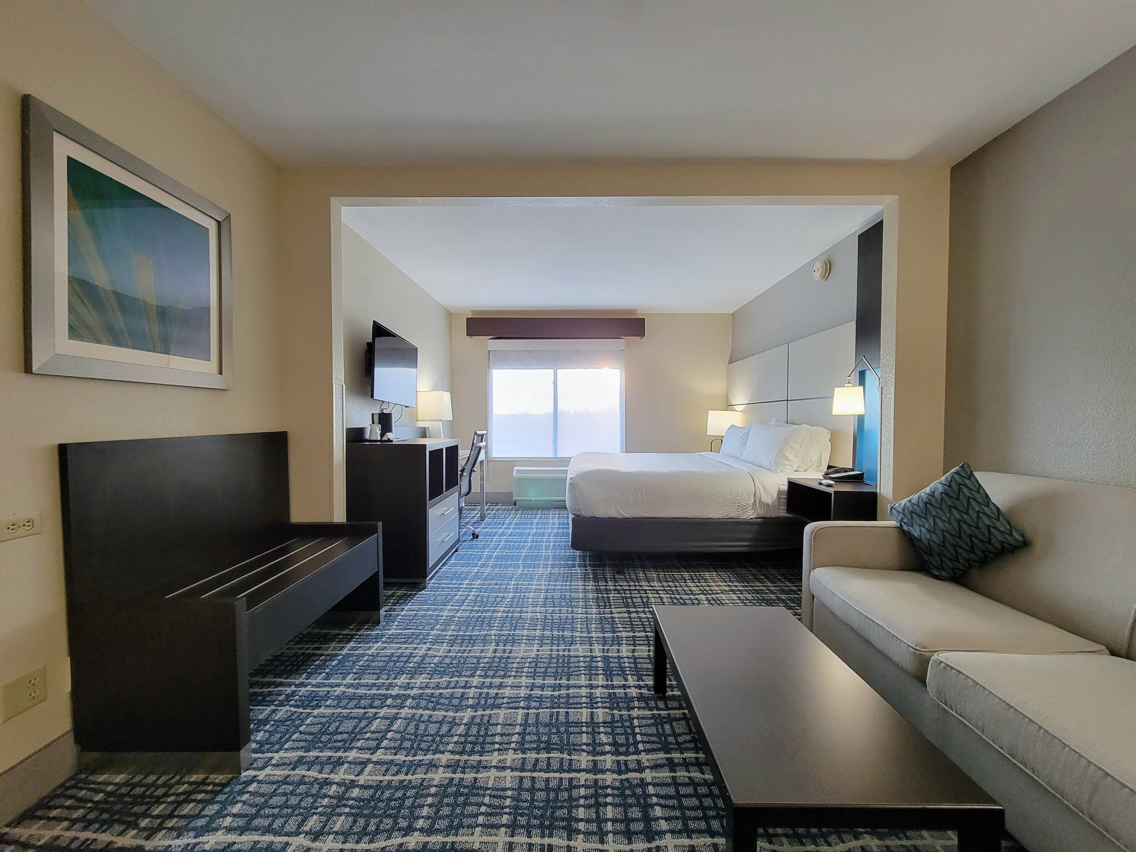 A hotel room with a bed, a sofa, a desk, a television, and a large window.