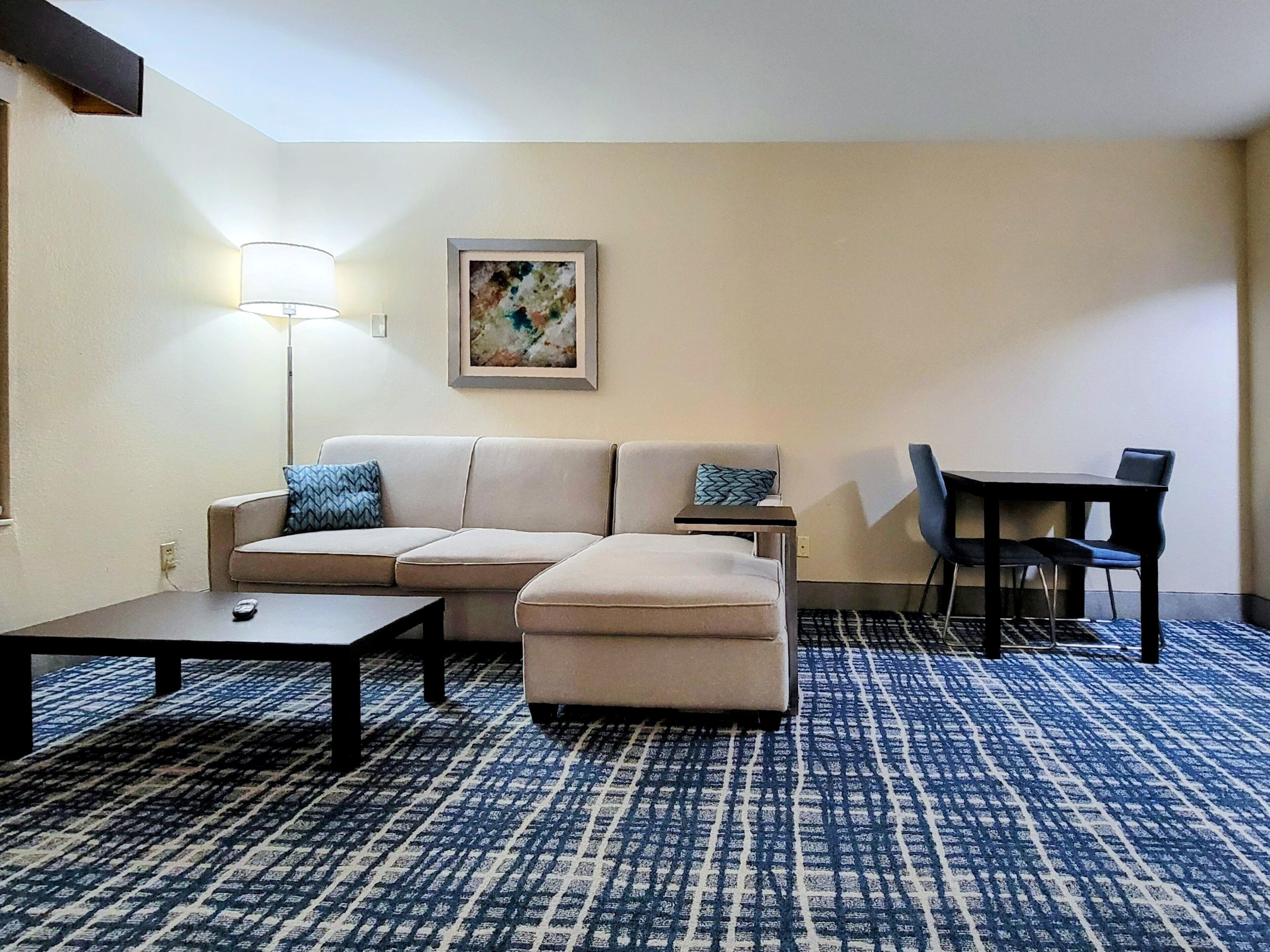 Une chambre d’hôtel avec un canapé, une petite table, un bureau avec des chaises et une moquette à motifs.
