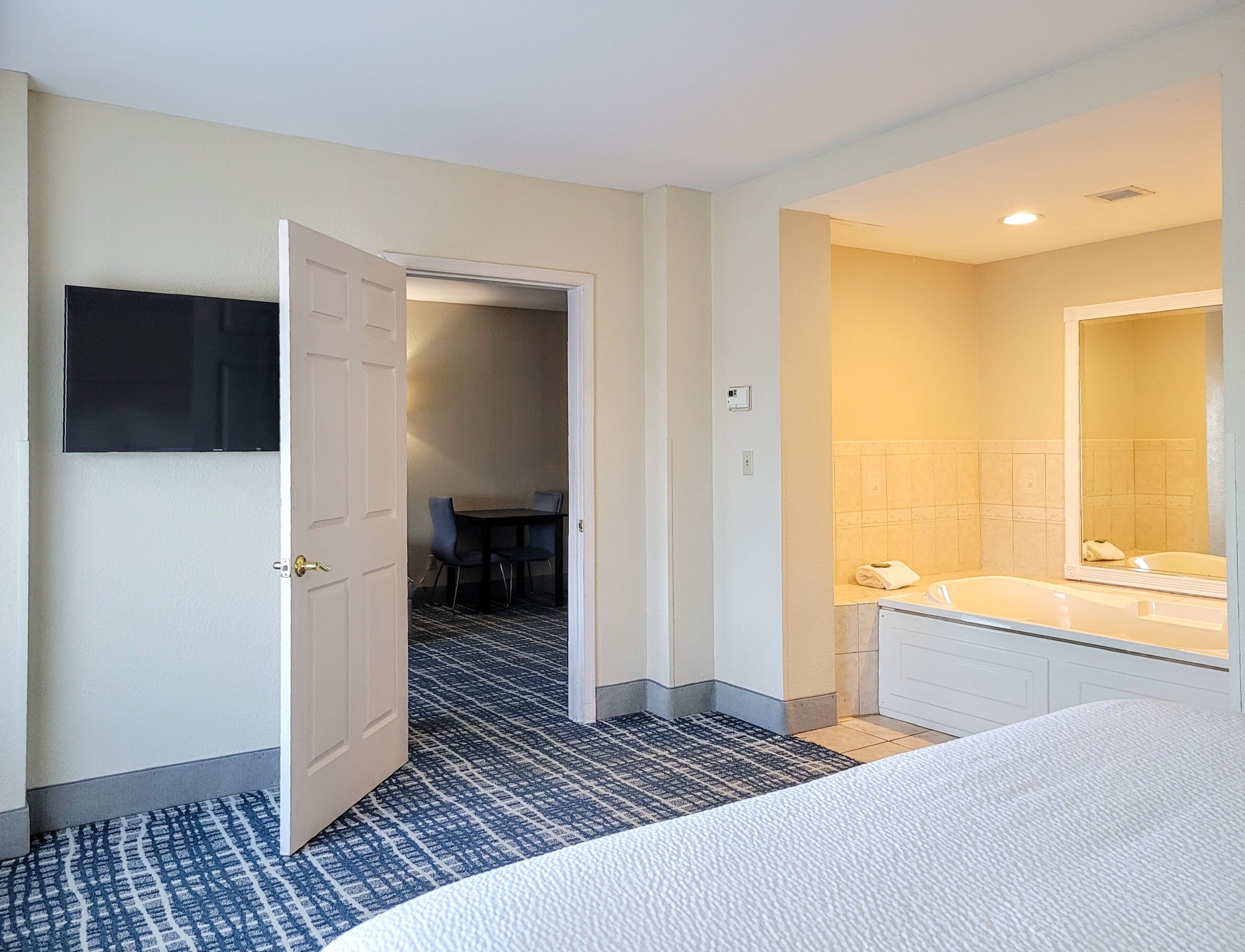 Hotelkamer met een bed, een badkamer met spiegel en wastafel, een aan de muur bevestigde televisie en een deur naar een eetgedeelte.