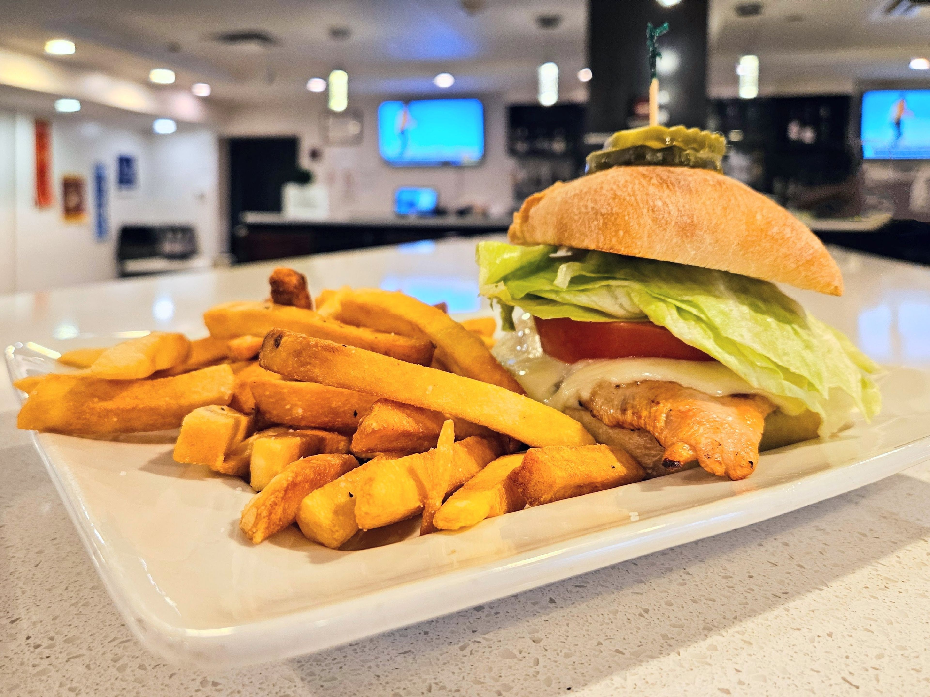 A plate with a sandwich and fries, a counter with a TV, and a blurred background with a sign.