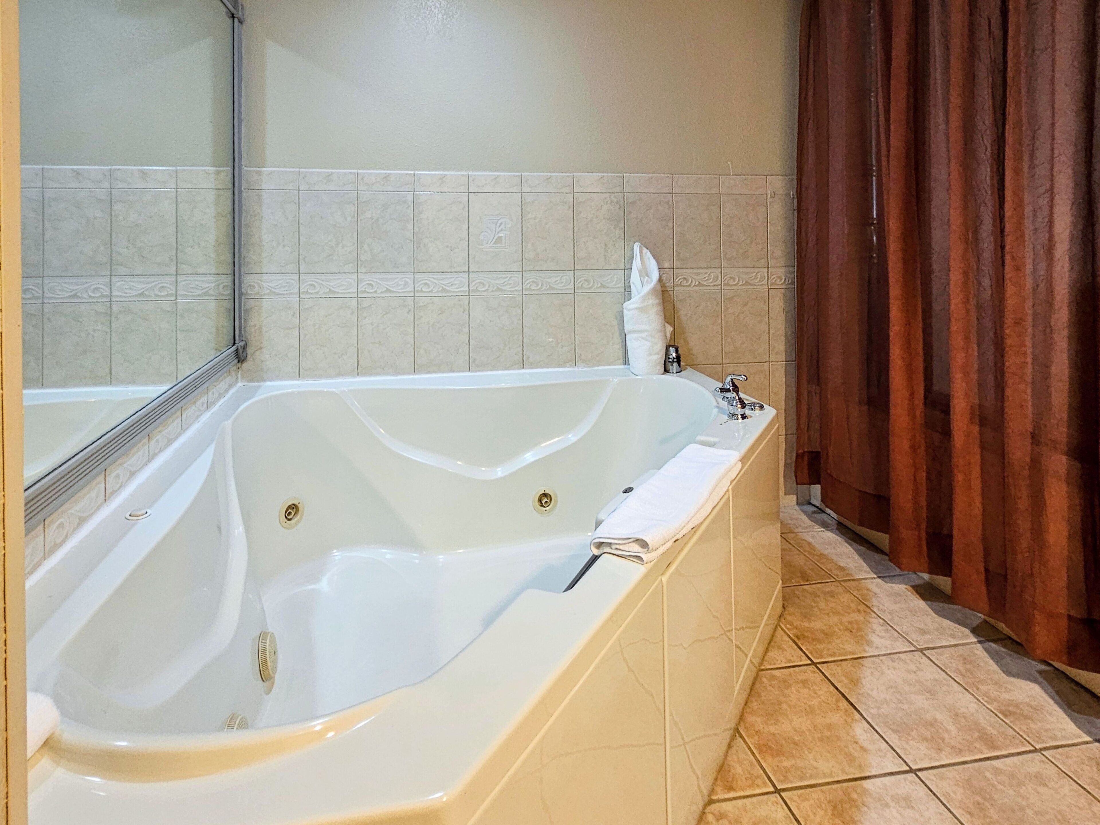 A large freestanding bathtub in a bathroom with beige tiles and a wooden curtain.