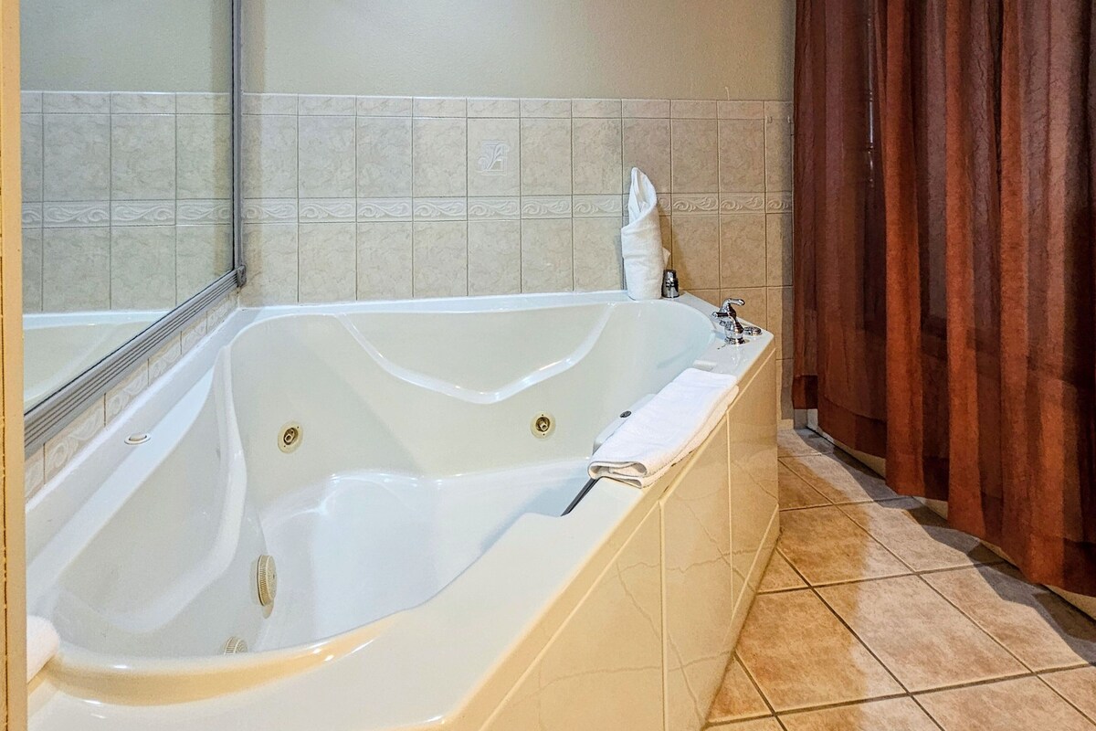 A large freestanding bathtub in a bathroom with beige tiles and a wooden curtain.