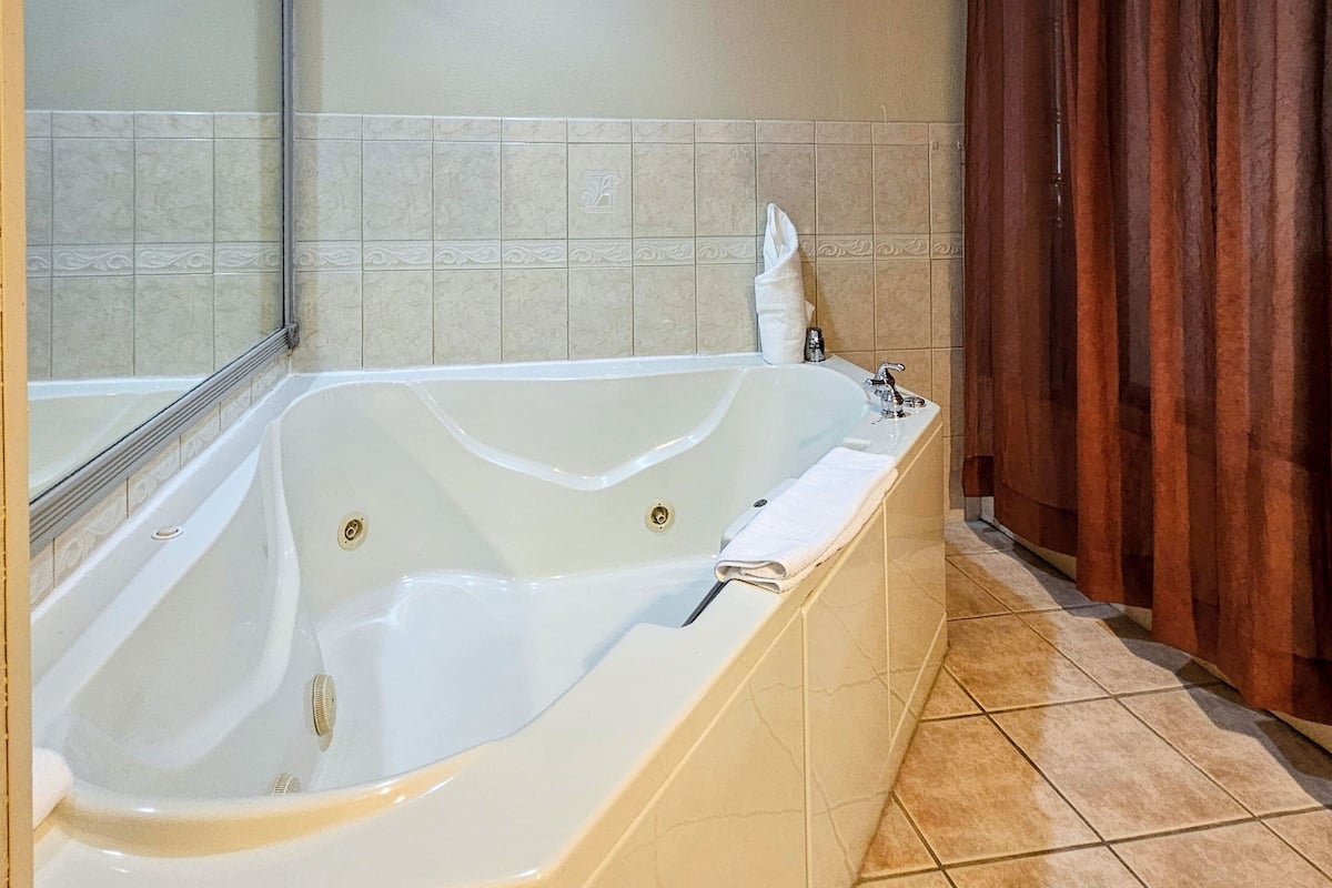 A large freestanding bathtub in a bathroom with beige tiles and a wooden curtain.