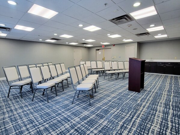 A conference room with rows of white chairs, a podium, and a patterned carpet.