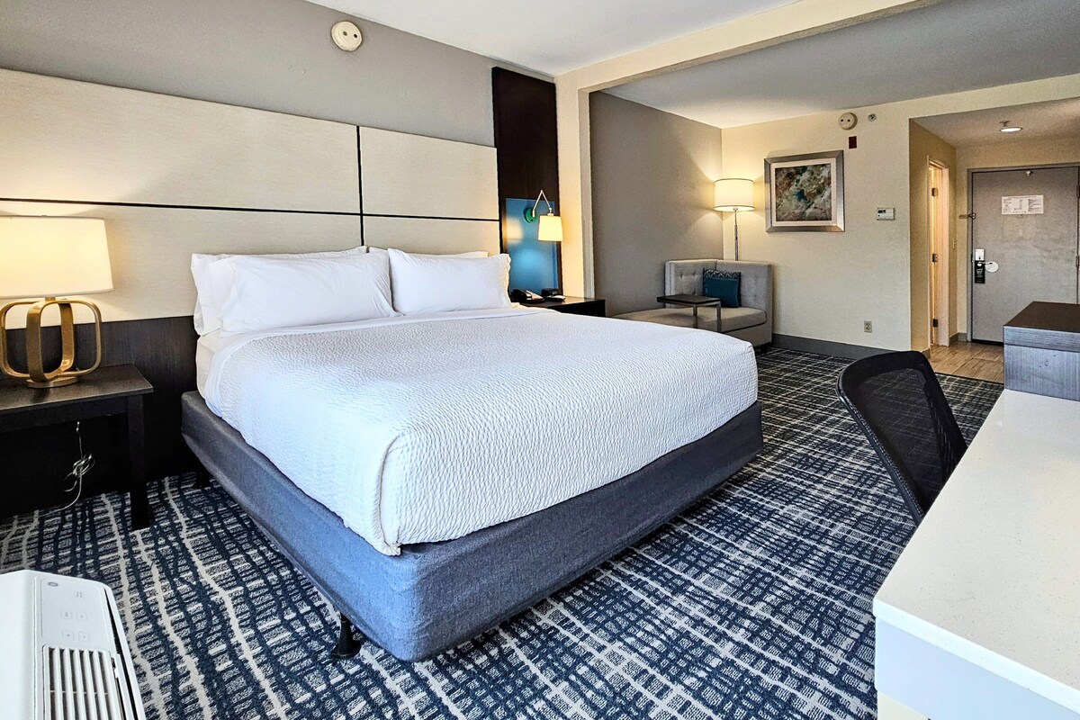 A hotel room with a large bed, a desk, a chair, a lamp, and a television.