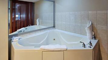 A large bathtub with a mirror above it, a sink, and a towel on the side.