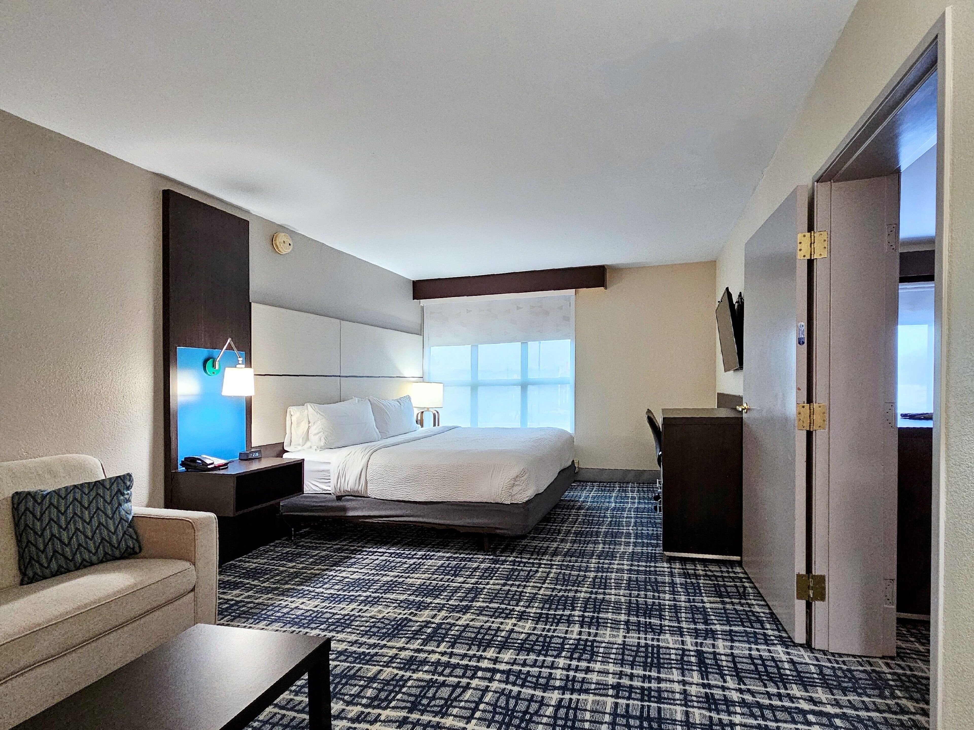 Une chambre d’hôtel équipée d’un lit, d’un bureau, d’une chaise, d’un canapé, d’une télévision et d’une moquette à motifs.