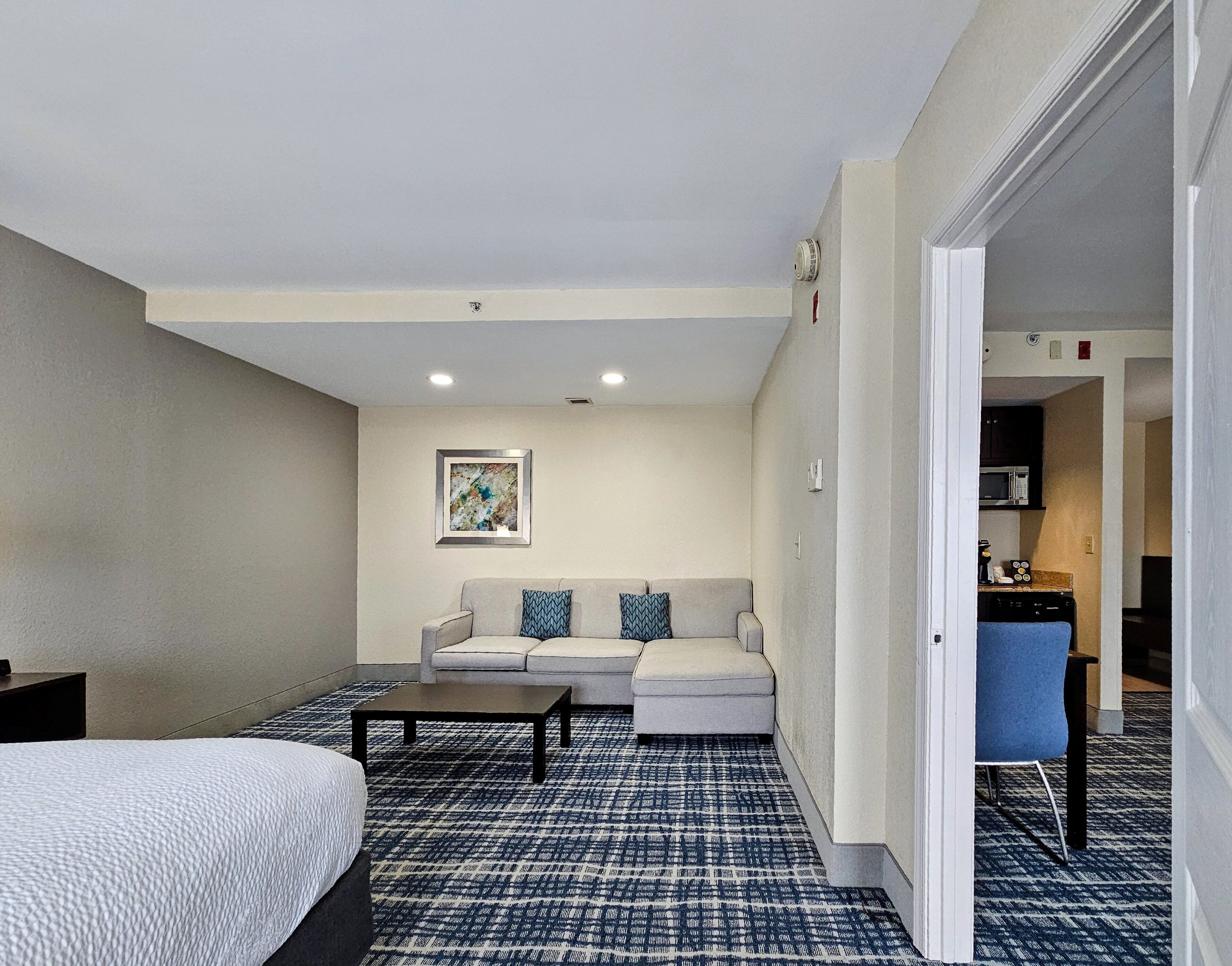 A hotel room with a bed, a sofa, a coffee table, and a patterned carpet.